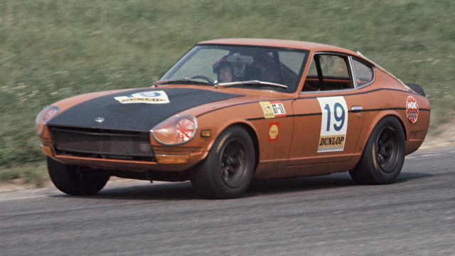 une Nissan Fairlady Z432-R (PS30-SB) orange avec le capot noir roule sur un circuit, vue de 3/4 avant gauche