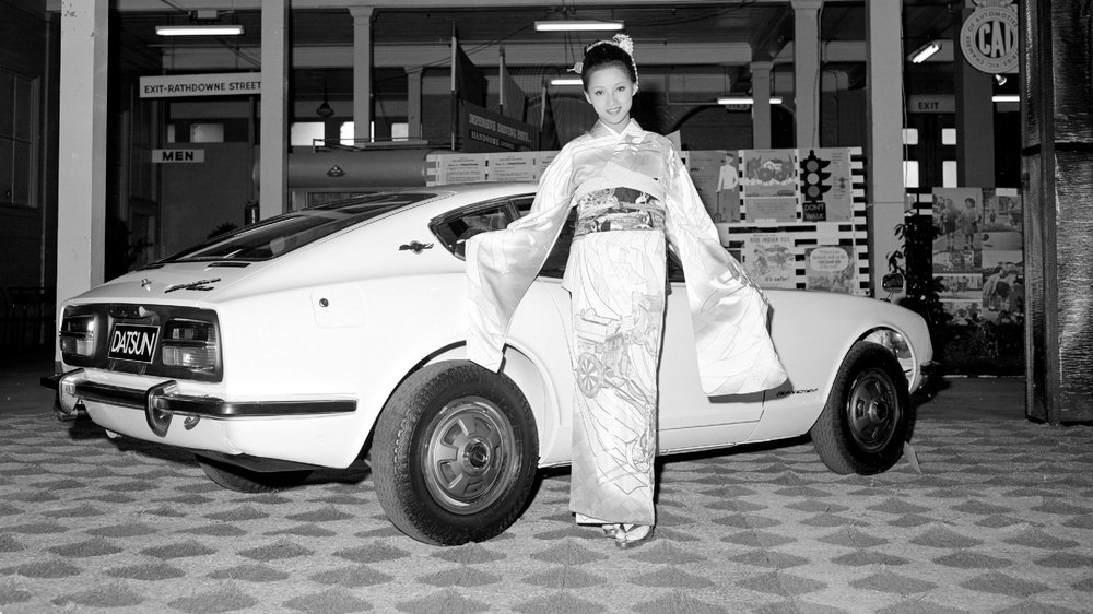 vue de 3/4 arrière droit. Une japonaise habillée en kimono présente la voiture